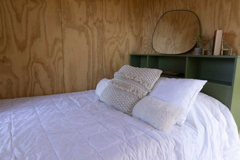 Bed in a Casita with white bedding and pillows against a wooden wall with a bookshelf.