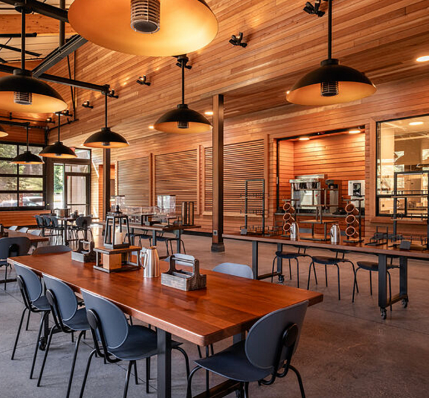 The dining hall at Enchanted Hills with wooden tables, chairs, and pendant lights.