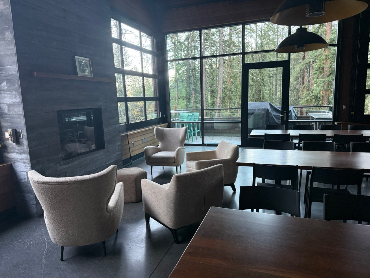 Modern interior with chairs, tables, and a fireplace near large windows with a view of trees.