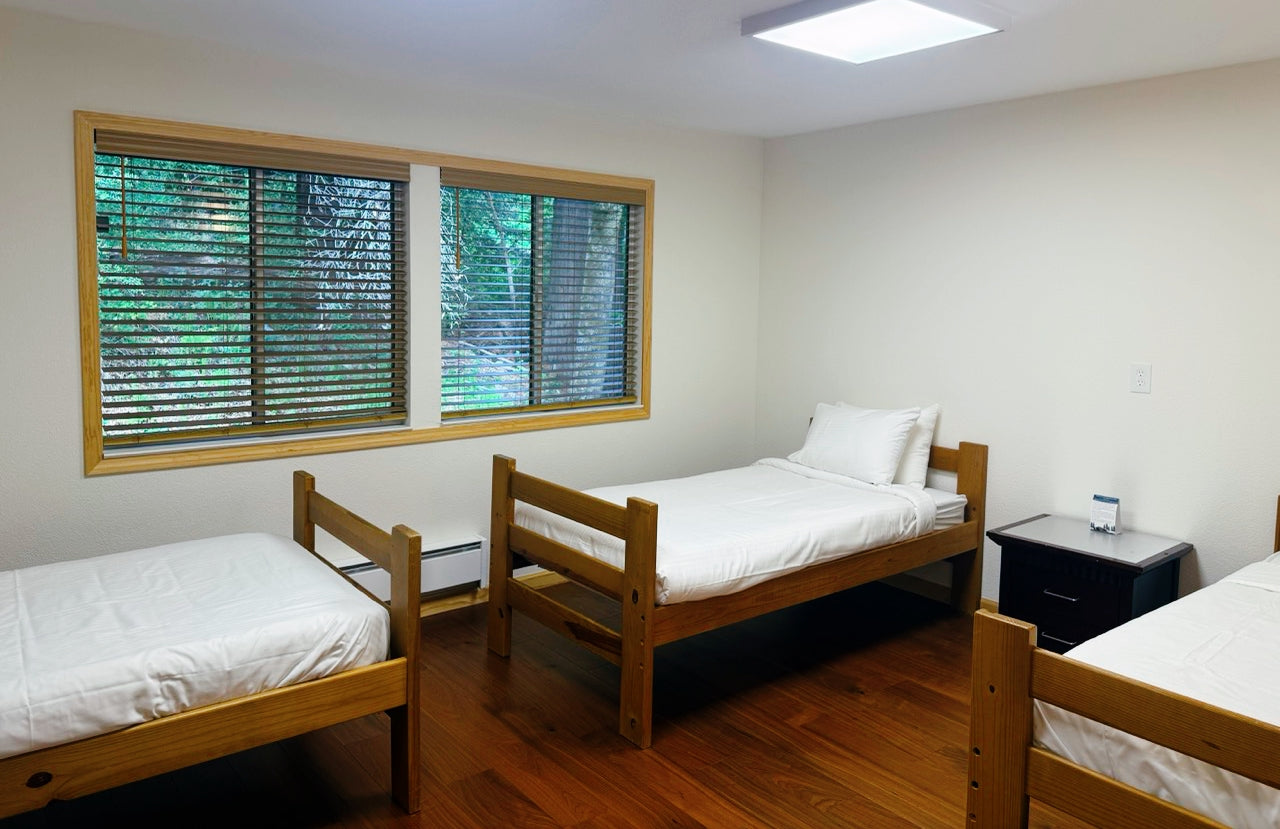 Three wooden twin beds in a room in the Lodge with a window and nightstands.